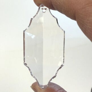 Clear faceted crystal pendant with scalloped edges, held between fingertips as a decorative ornament