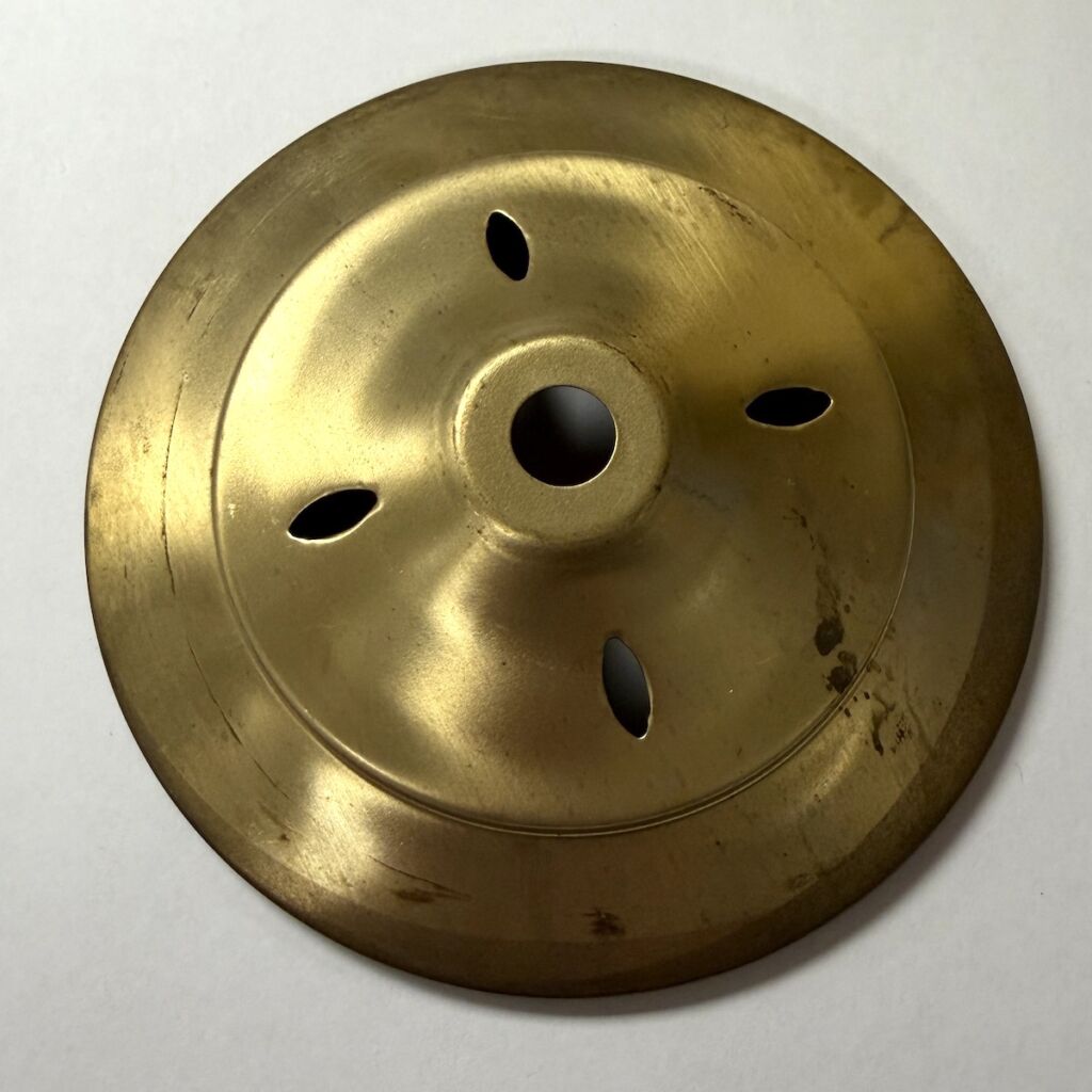 Brass circular metal plate with a central hole and four elongated nearby holes in a symmetrical pattern.