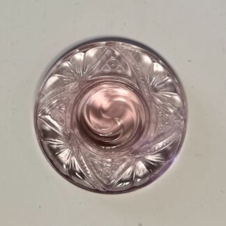 Top-down view of a pink cut-glass dish with a swirled center and starburst patterns around the rim.