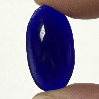 A cobalt blue, translucent glass bead held sideways between two fingers.